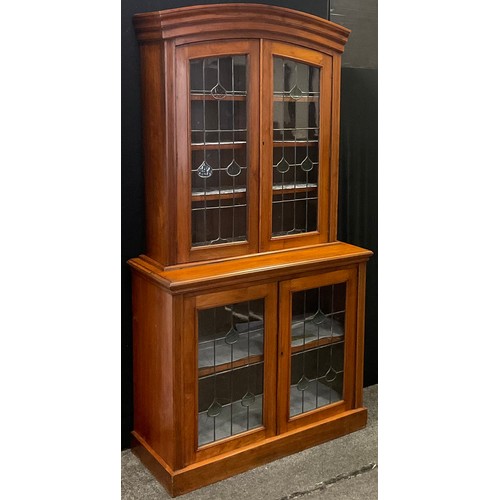 155 - An Arts & Crafts walnut display cabinet, arched pediment above two leaded stained and clear glass do... 