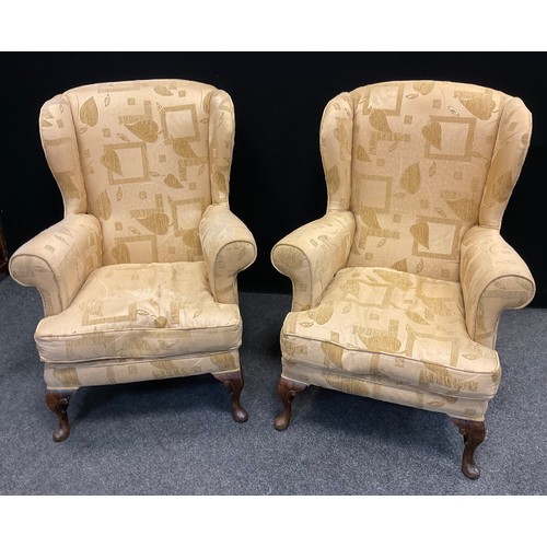 200 - A pair of wingback armchairs, upholstered in a cream textured floral and box patterned fabric, carve... 