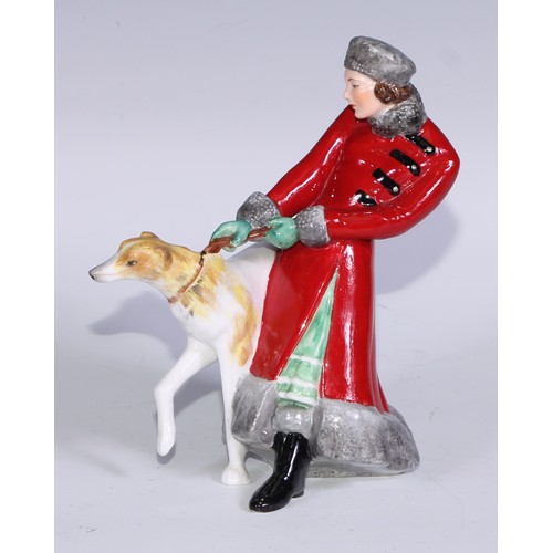 634 - A Royal Crown Derby figure, Olga, she stands, wearing a fur trimmed red trench coat holding a Borzoi... 