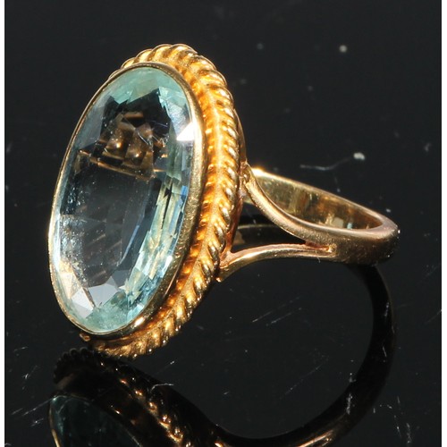 246 - An aquamarine and gold coloured metal ring, single large oval facet cut stone, within a gadrooned mo... 