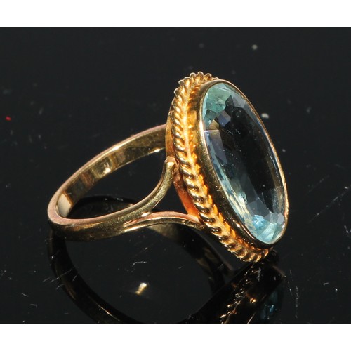 246 - An aquamarine and gold coloured metal ring, single large oval facet cut stone, within a gadrooned mo... 