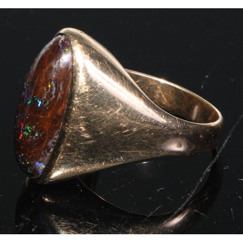 154 - A black opal and 9ct gold ring, the large elongated oval cabochon stone set within within a plain sh... 