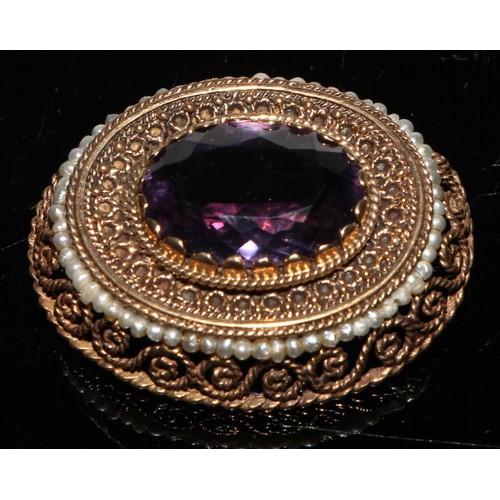 235 - A Victorian style amethyst and gold coloured metal oval brooch, the central faceted within open fili... 