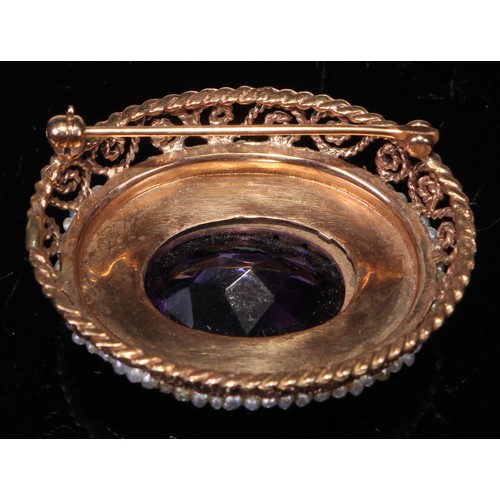 235 - A Victorian style amethyst and gold coloured metal oval brooch, the central faceted within open fili... 