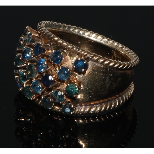 211 - A sapphire cluster ring, arched tapering shank adorned with twenty three blue sapphires, yellow meta... 