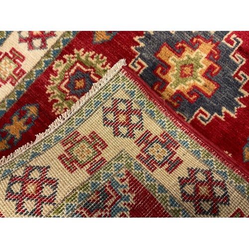 63 - A Kazak small runner carpet / rug, multiple medallions within a field of light red, enclosed within ... 