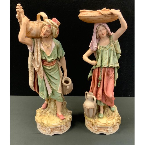 13 - A pair of Royal Dux figures, Persian Water Carriers, both standing, in washed tones, picked out in g... 