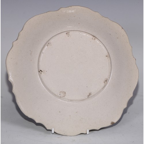 534 - An 18th century salt glazed stoneware shaped circular plate, moulded in the Rococo taste with leafy ... 