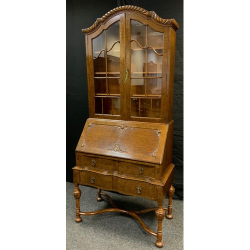 33 - A mid 20th century oak bureau bookcase, serpentine top with pair of glazed doors, three tiers of she... 