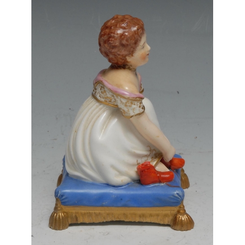 20 - A Bloor Derby figure, of a young child putting on her boots, on a tasselled  blue cushion, 9cm high,... 