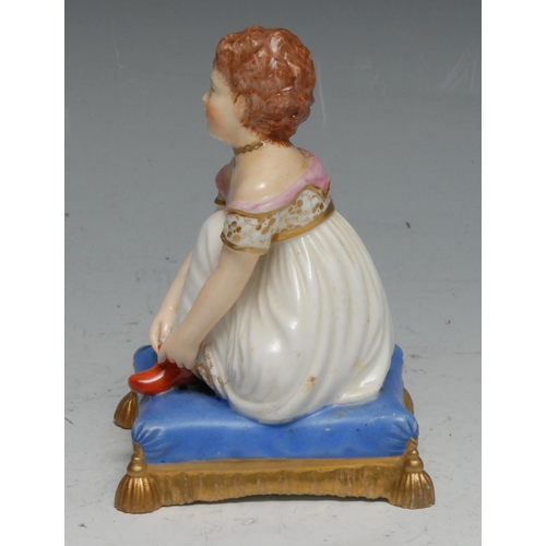 20 - A Bloor Derby figure, of a young child putting on her boots, on a tasselled  blue cushion, 9cm high,... 