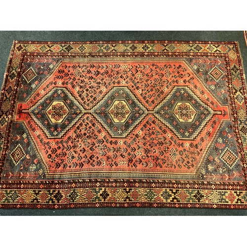 73 - A large Qashgai rug, hand knotted in muted tones of blue, red, and burgundy, with a row of three dia... 