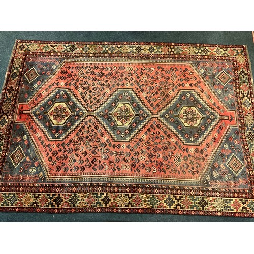 73 - A large Qashgai rug, hand knotted in muted tones of blue, red, and burgundy, with a row of three dia... 