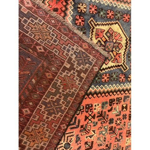 73 - A large Qashgai rug, hand knotted in muted tones of blue, red, and burgundy, with a row of three dia... 