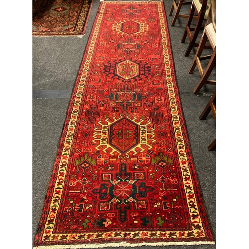 77 - A Heriz runner carpet, hand knotted in red, black, cream, and green, with a row of three hexagonal m... 