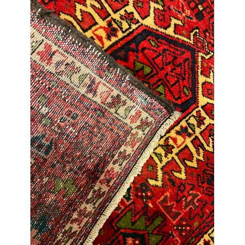 77 - A Heriz runner carpet, hand knotted in red, black, cream, and green, with a row of three hexagonal m... 