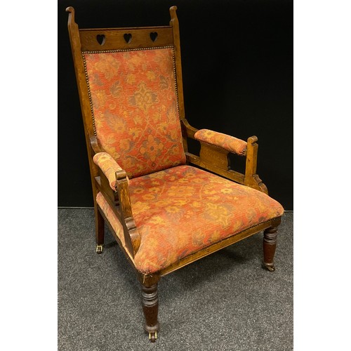 84 - An Arts and Crafts oak library chair, the upholstered back with heart pierced cresting rail, over st... 