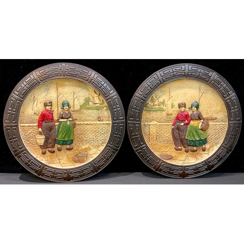 91 - A pair of Bretby Pottery Dutch pattern circular wall chargers, decorated in low relief with figures ... 