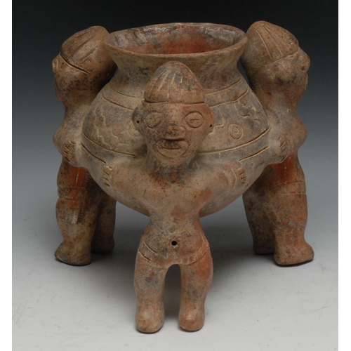 25 - A South American terracotta vessel, with three figures standing holding a vase, 23cm high