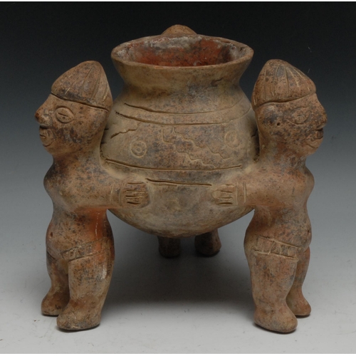 25 - A South American terracotta vessel, with three figures standing holding a vase, 23cm high