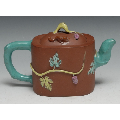 306 - A Chinese Yixing rounded rectangular wine pot moulded and picked out in coloured enamels with fruiti... 