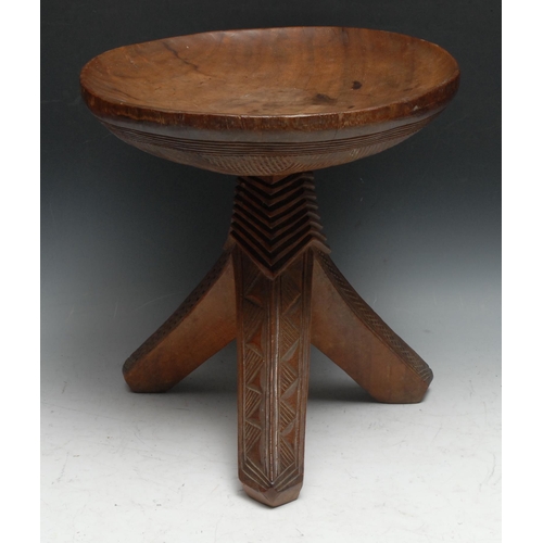 733 - Tribal Art - an Igbo stool, dished circular top above three outswept legs carved with geometric moti... 