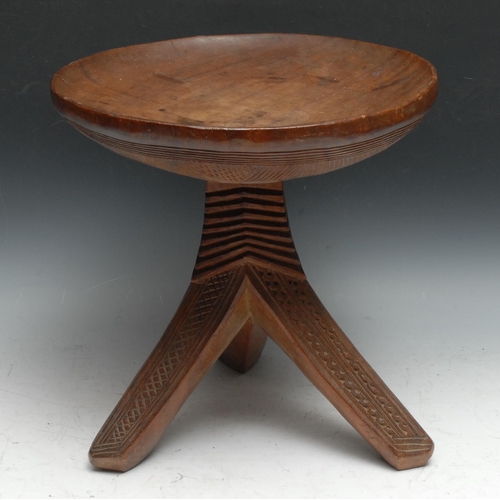 733 - Tribal Art - an Igbo stool, dished circular top above three outswept legs carved with geometric moti... 