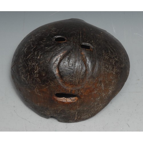 720 - Tribal Art - a coconut shell mask, abstract features, pierced eyes and mouth, 13.5cm wide, probably ... 