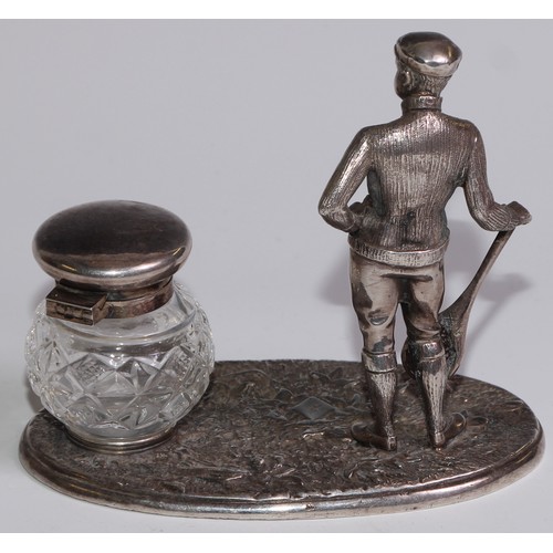 462 - A silver plated novelty inkstand, as a gentleman dressed for tennis, glass well, 12.5cm wide