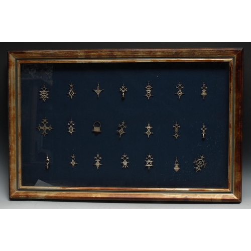 125 - A collection of Tuareg silvered agadez crosses, various forms, Niger, framed, the arrangement 48cm x... 