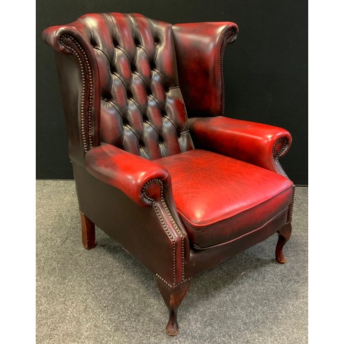 49 - A Chesterfield wing-back armchair, deep button back, sang de bouef red leather, cabriole legs, 102cm... 