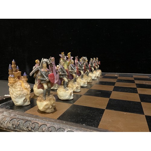 23 - A novelty chess set, the resin pieces as myth and magic figures, the chess board with a pair of stor... 