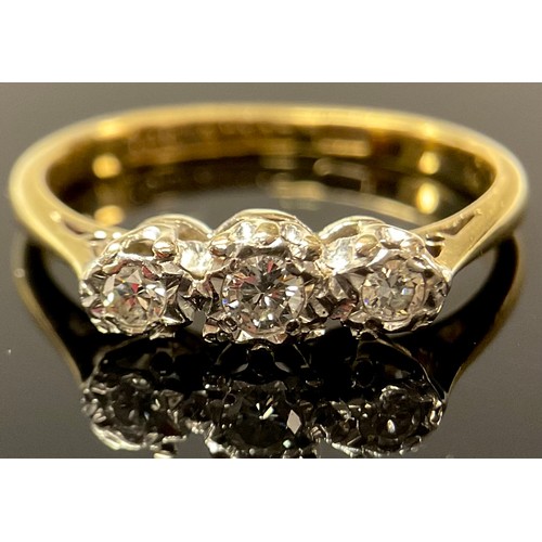 557 - An 18ct gold three stone diamond ring, the graduated brilliant cut stones illusion set in platinum, ... 