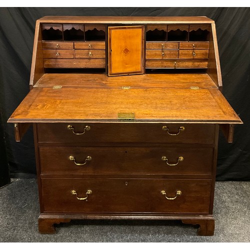 135 - A George III oak bureau, the fall front enclosing an arrangement of small drawers, pigeon holes and ... 