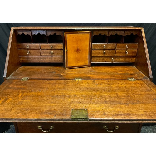 135 - A George III oak bureau, the fall front enclosing an arrangement of small drawers, pigeon holes and ... 