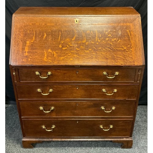 135 - A George III oak bureau, the fall front enclosing an arrangement of small drawers, pigeon holes and ... 