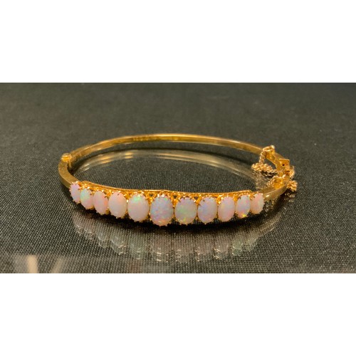 748 - An opal hinge bangle, set with eleven oval graduated opal cabochons, ranging from approx 7mm x 1.5mm... 