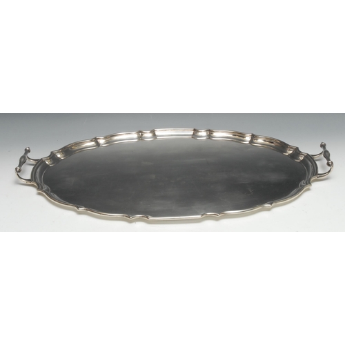 149 - A George V silver shaped oval two-handled serving tray, piecrust border, plain field, 66cm over hand... 