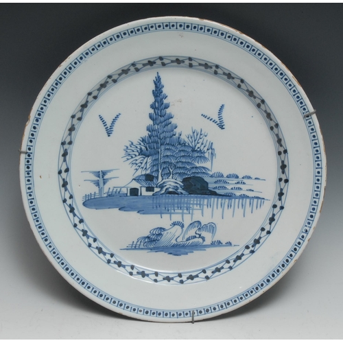 794 - An 18th century Delft circular charger, painted in tones of blue with a house, trees and rocks, 35cm... 