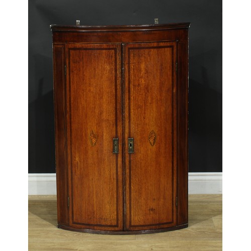 1242 - A George III oak and mahogany bowfront corner cupboard, outswept cornice above a pair of crossbanded... 