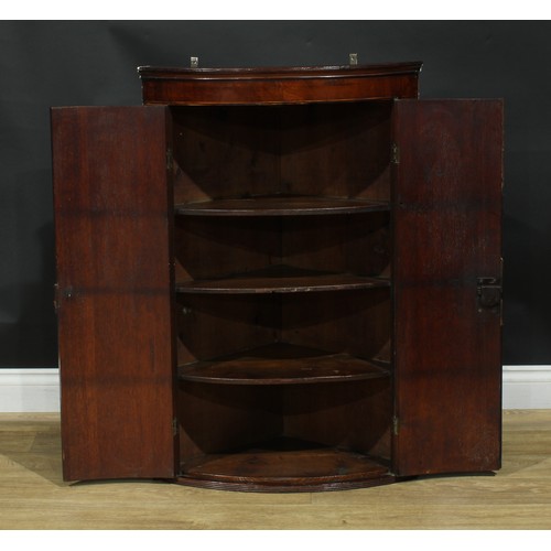 1242 - A George III oak and mahogany bowfront corner cupboard, outswept cornice above a pair of crossbanded... 