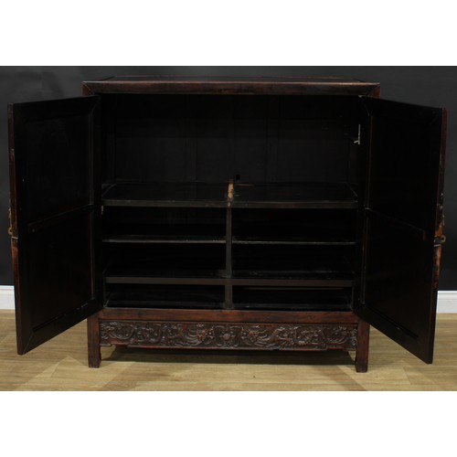 1043 - A Chinese hardwood side cabinet, flush rectangular top above a pair of panel doors carved with duell... 