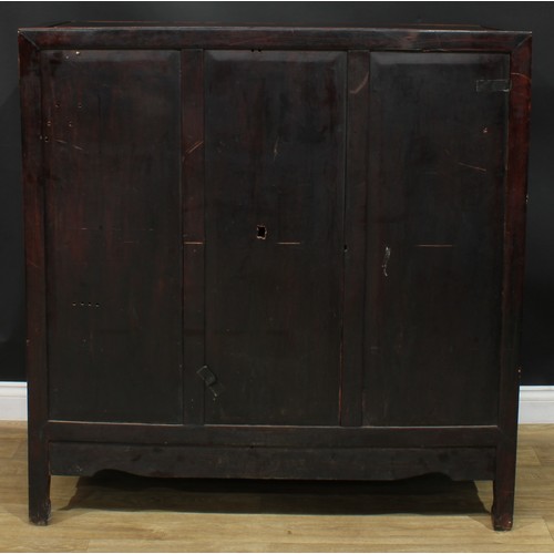 1043 - A Chinese hardwood side cabinet, flush rectangular top above a pair of panel doors carved with duell... 