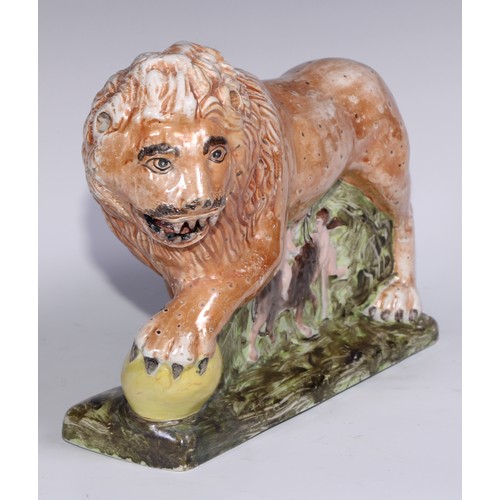 445 - A large pearlware model of a lion, he stands, roaring, his paw upon a sphere, the base moulded with ... 