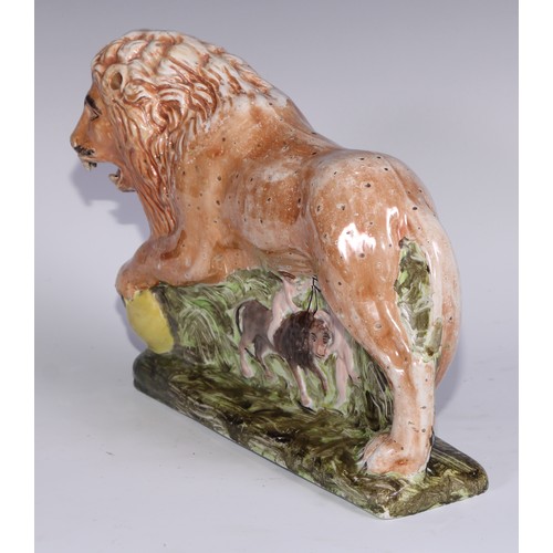 445 - A large pearlware model of a lion, he stands, roaring, his paw upon a sphere, the base moulded with ... 