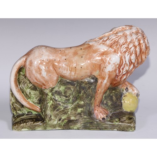 445 - A large pearlware model of a lion, he stands, roaring, his paw upon a sphere, the base moulded with ... 