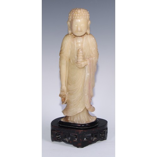 799 - A Chinese soapstone figure, carved as Buddha holding a pagoda, carved hardwood stand, 41cm high, ear... 