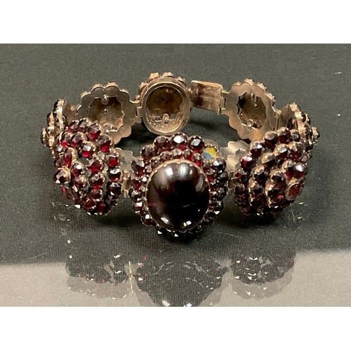 446 - A 19th century deep red garnet cabochon and faceted eight panel bracelet, unmarked gold coloured met... 