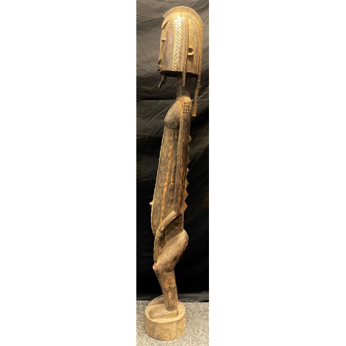 18 - A carved tribal standing figure, probably Senufo, as a male with shaped headdress, beard,  zigzag an... 