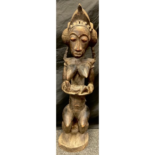 21 - An African Yoruba carved fertility figure, as a seated female, cradling a feeding baby, 93cm high